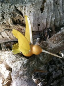 A carved gourd resembling a hummingbird sits displayed on a wood burl
