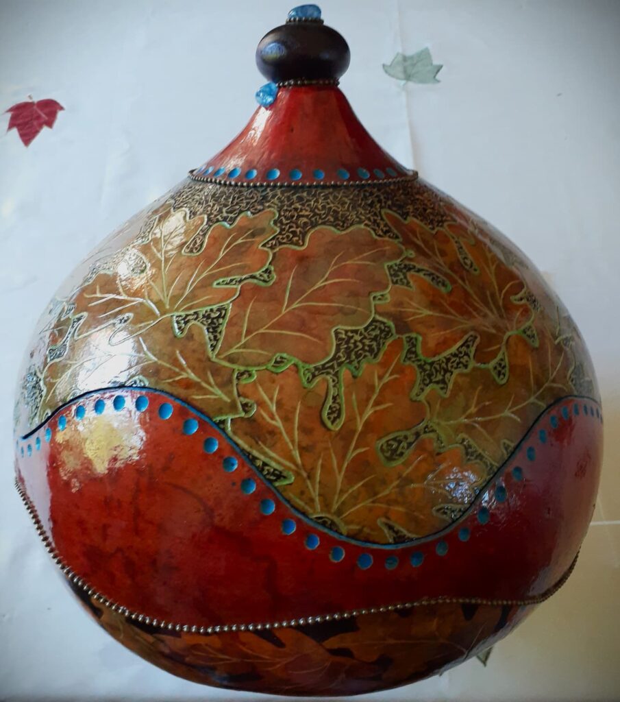A large decorative gourd that has been carved and painted to look like leaves